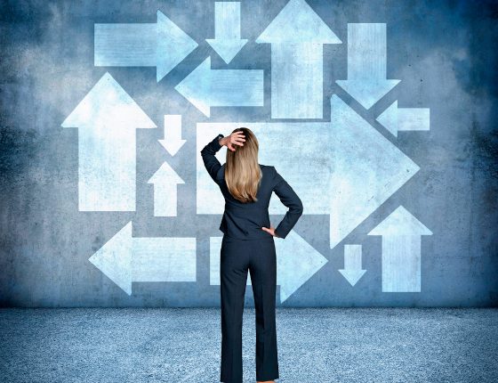 Confused Businesswoman Looking At Arrows Pointing In Different Directions